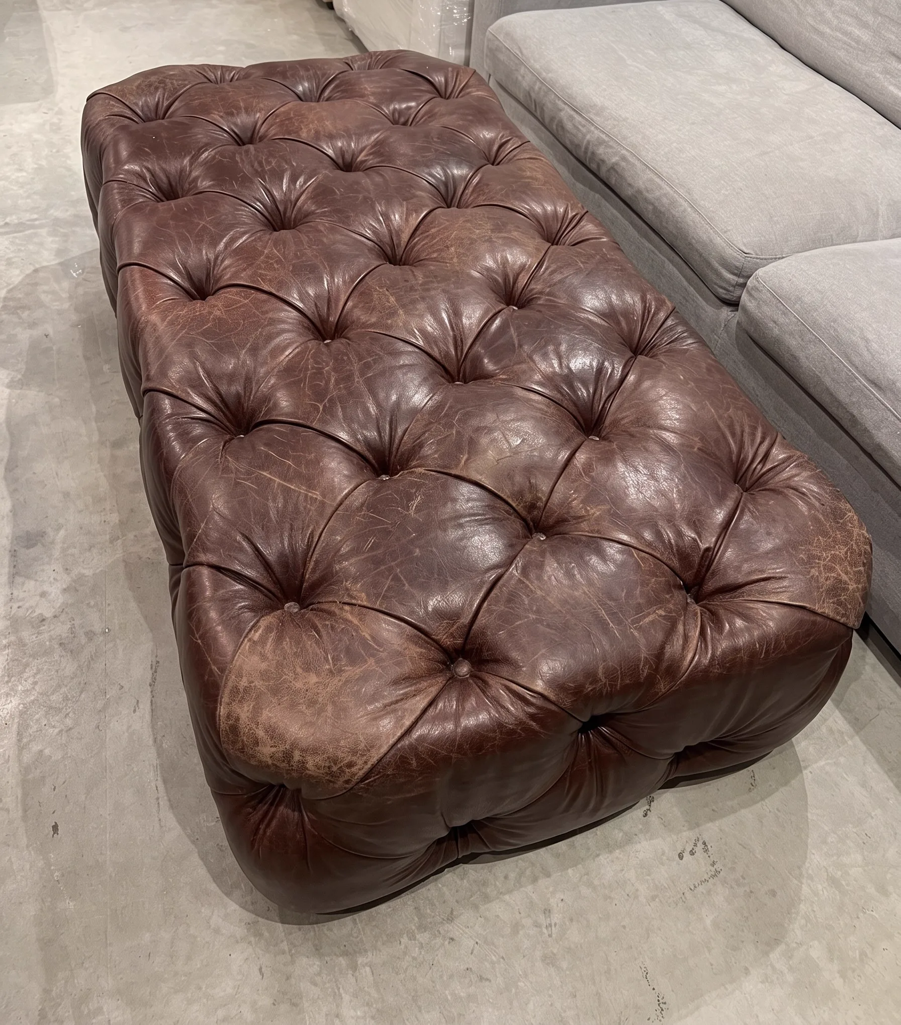 Worn, abraded dark-brown buttoned leather ottoman before restoration